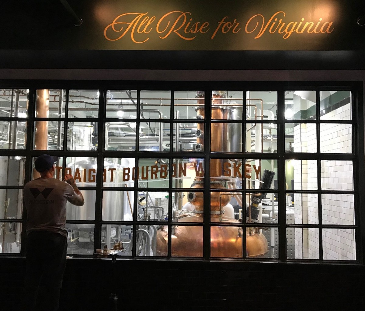A man paints the words "Straight Bourbon Whiskey" on the windows of the Tarnished Truth Distilling Company.